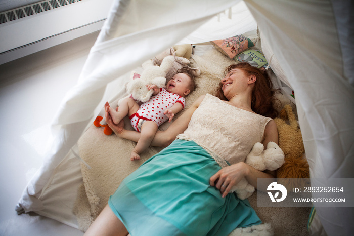 Mother playing with baby girl in tent at home