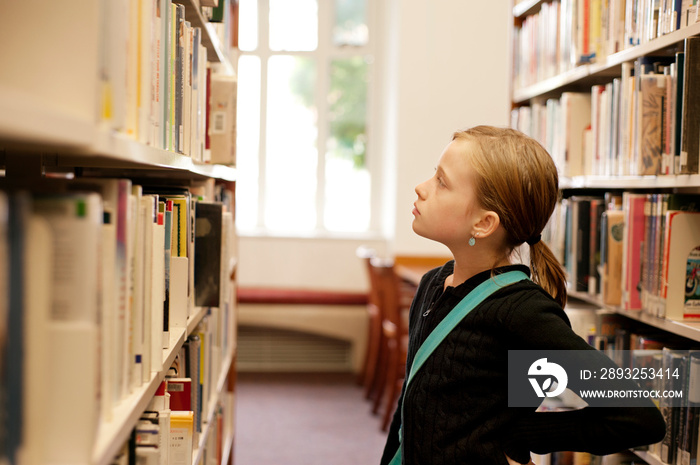 Girl looking at books in shelves at library