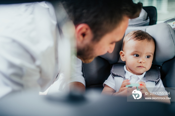 Portrait of caring young father and baby boy enjoying car transportation with child seat