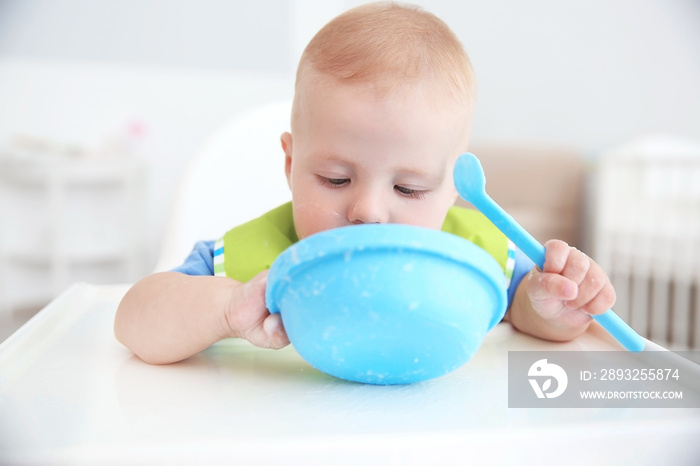小婴儿在室内用勺子从碗里吃东西