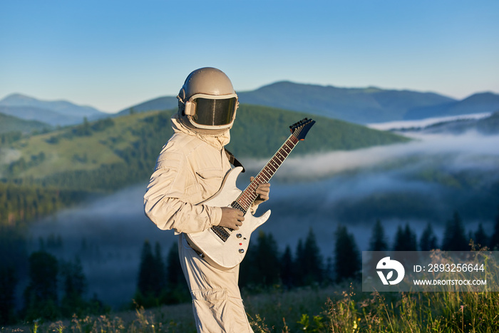 Horizontal side view portrait of a spaceman wearing white space suit and a helmet holding white guit