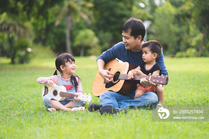 Asian father and daughter are playing guitar and ukulele together and the little baby boy sitting wi