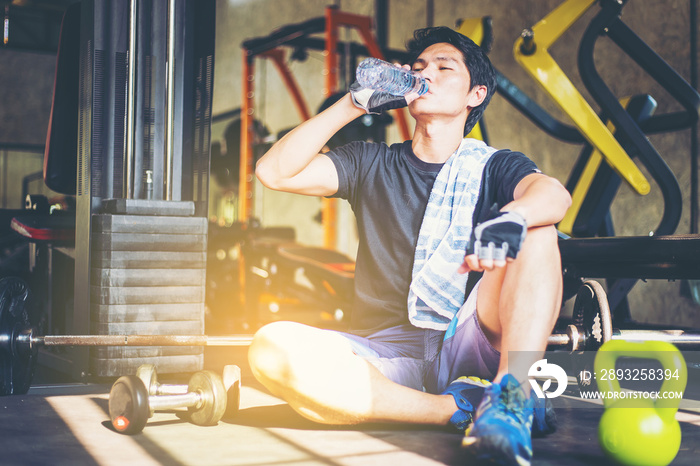 Fitness man drinking water from bottle. Muscular young male at gym taking a break from workout.