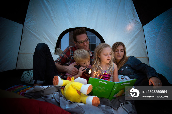 Parents and children (6-7) reading book in tent