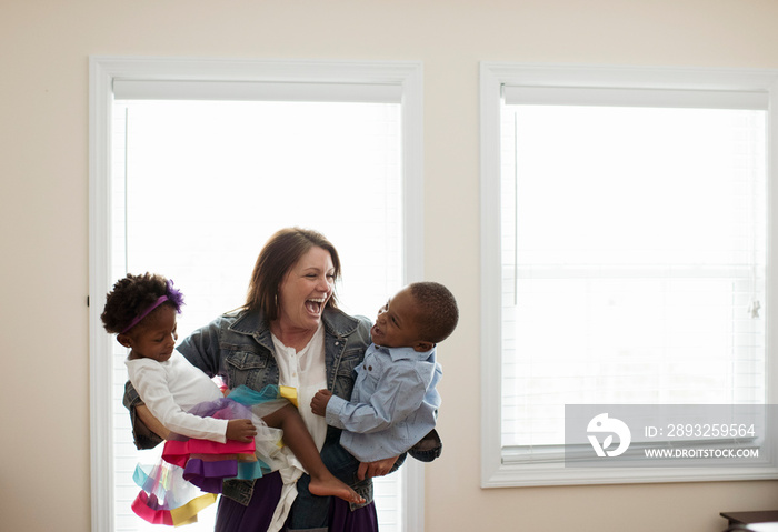 Happy mother carrying children while standing against windows at home