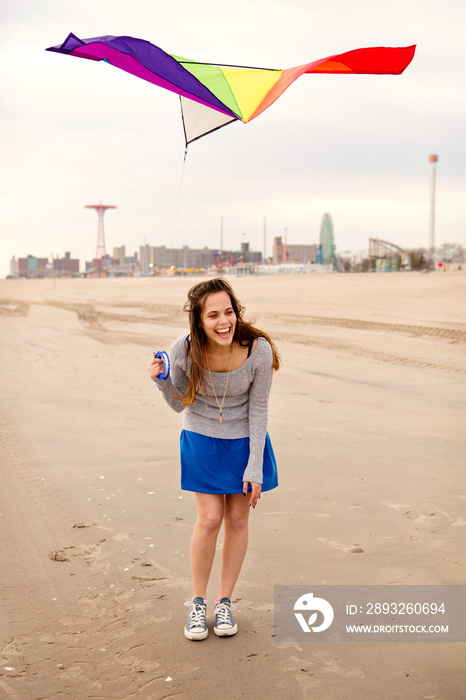 Laughing young woman flying kite on beach