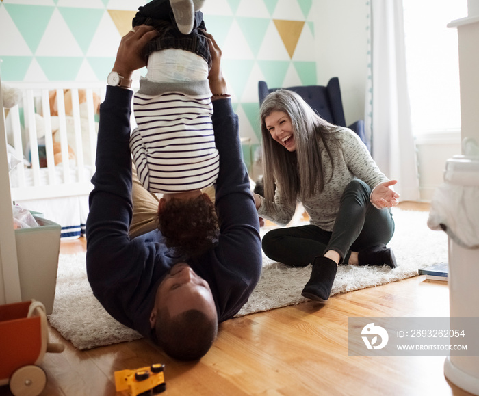 Happy mother looking at father playing with son while sitting in room