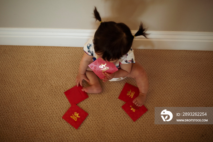 High angle view of baby girl holding red envelopes while sitting on rug at home