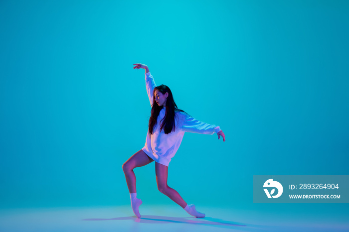 Inspired. Young and graceful ballet dancer isolated on blue studio background in neon light. Art, mo