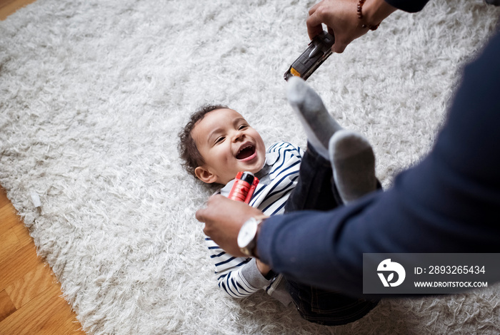 Cropped hands of father showing toys to happy son lying on rug at home