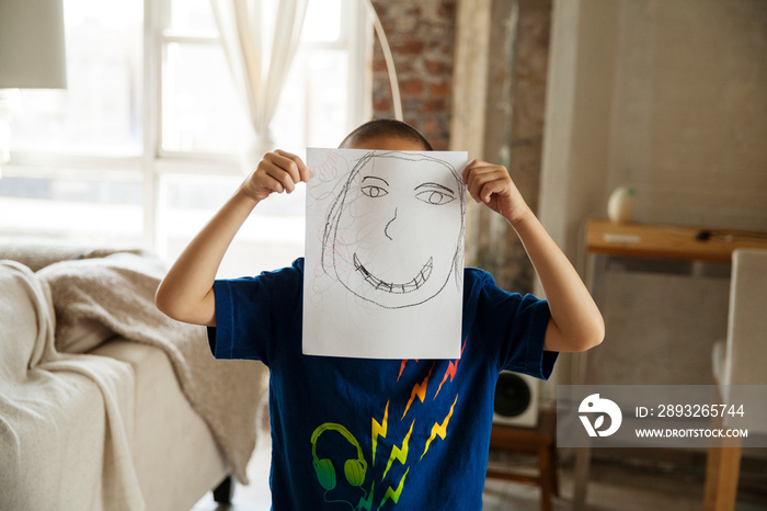 Boy (6-7) holding paper card with painted face