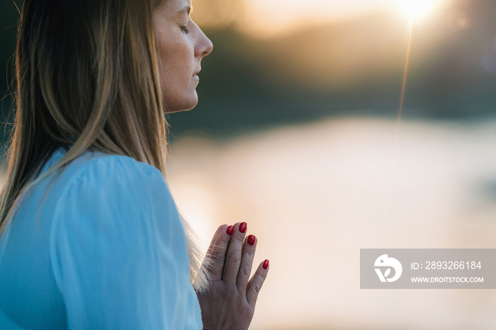 Sunset Meditation. Woman Meditating by the Lake in Prayer Position.