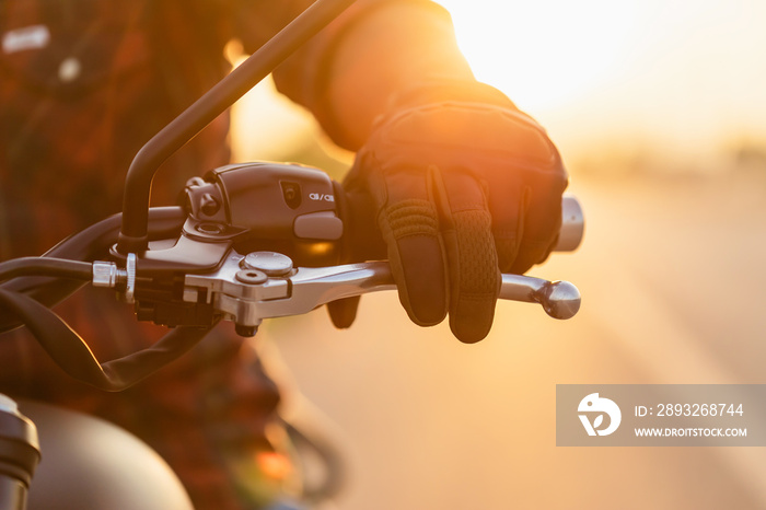 Macro left hand of motorcyclist wearing riding glove on the clutch. Outdoor shooting on the road wit