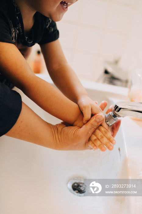 Cropped image of mother washing sons hands in bathroom sink