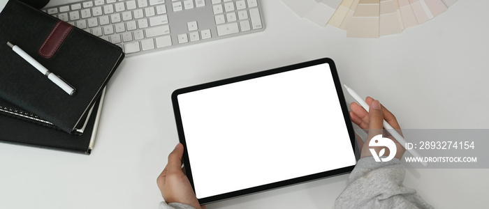 Top view of female graphic designer using tablet with colour swatches on white table.