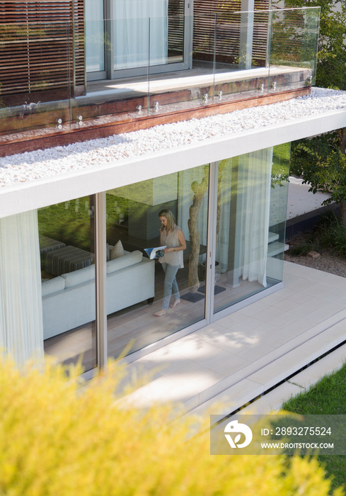 Woman reading book at window of luxury modern house