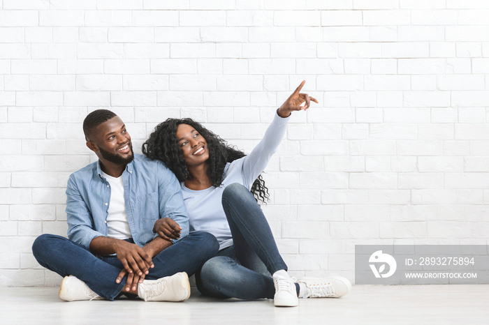 Thoughtful couple sitting on floor at new house, looking aside