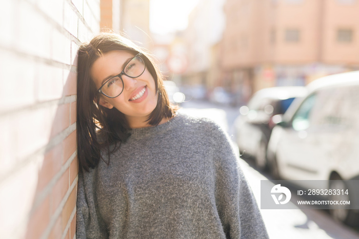 Beautiful young woman wearing glasses smiling cheerful leaning on bricks wall, casual pretty girl at