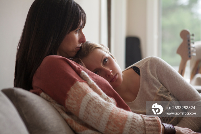 Daughter leaning mothers shoulder while sitting on sofa