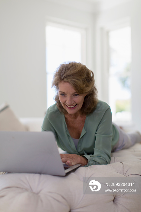 Smiling senior woman using laptop on ottoman