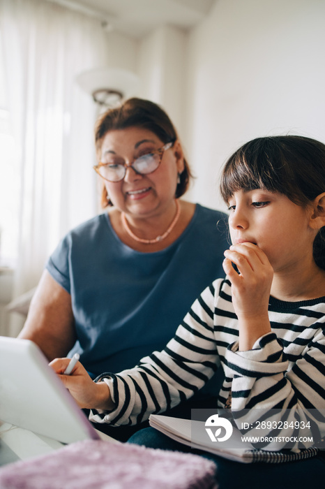 Grandmother assisting girl in homework on digital tablet at home