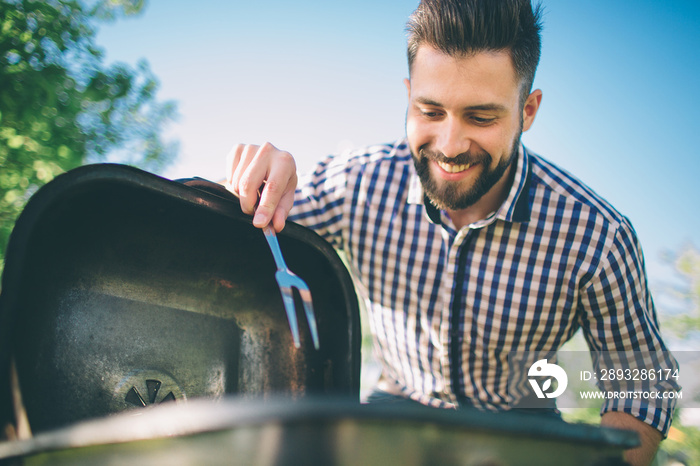 Handsome man preparing barbecue for friends. man cooking meat on barbecue - Chef putting some sausag