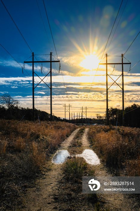 Sunrise over the electric poles and easement footpath with frozen puddles after winter rain. Dramati