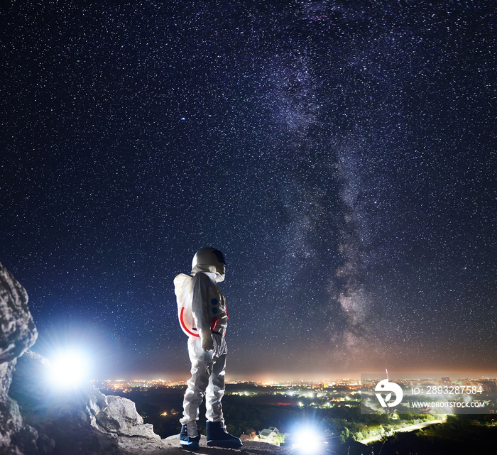 任务专家宇航员站在岩石山上，看着乳白色的星空