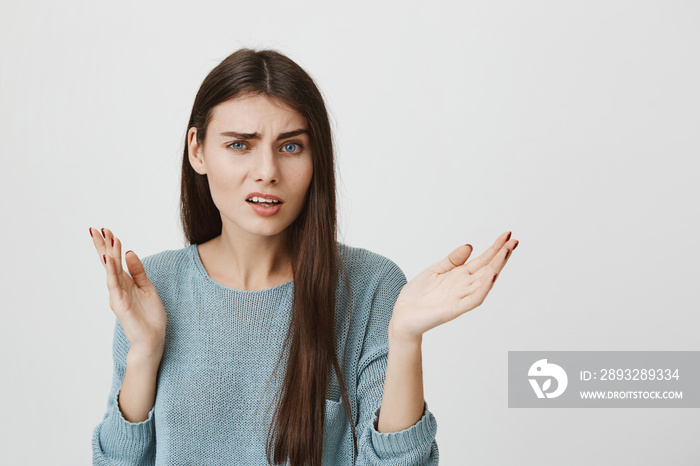 Headshot of clueless young caucasian brunette woman looking at camera with confused and puzzled expr