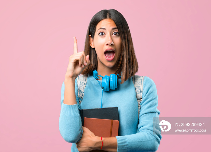 Young student girl with blue sweater and headphones standing and thinking an idea pointing the finge