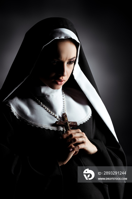 beautiful young worried nun holding cross on grey