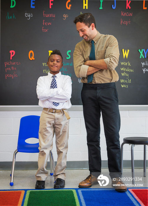 Portrait of teacher and schoolboy (8-9) standing before blackboard posing with arms crossed