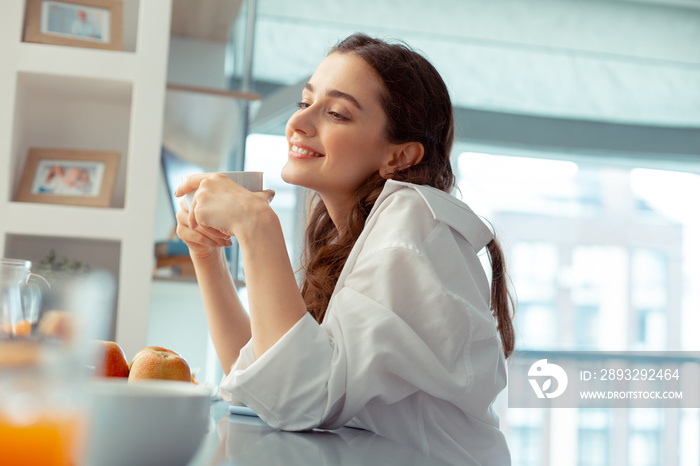 Woman wearing white shirt feeling relaxed drinking coffee