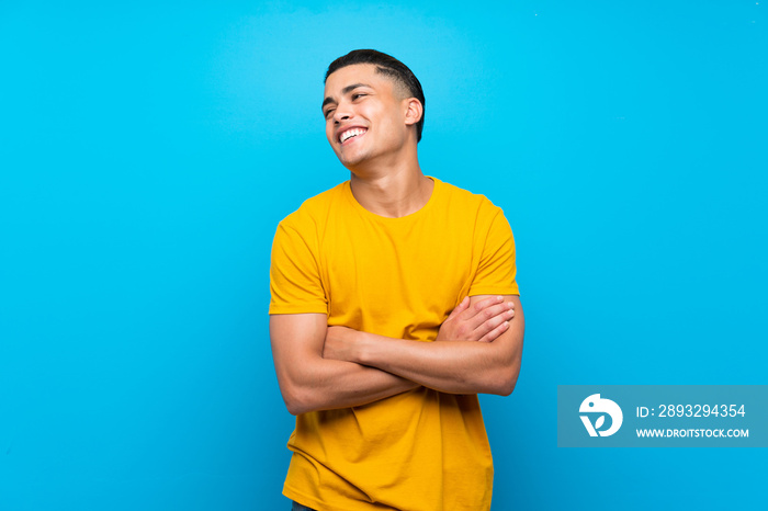 Young man with yellow shirt over isolated blue background happy and smiling