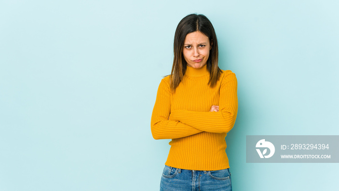 Young woman isolated on blue background frowning face in displeasure, keeps arms folded.