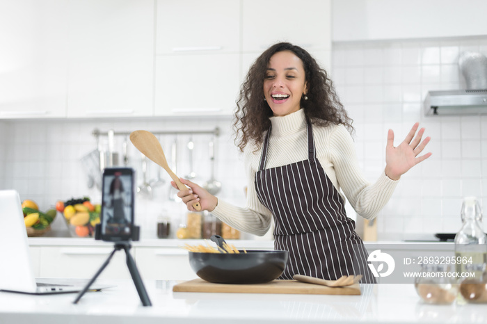 拉丁女性在家厨房做饭时，用智能手机在线直播。