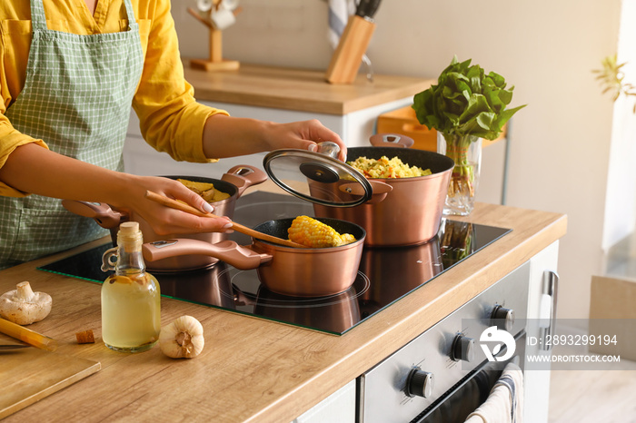 Woman in apron preparing corn cobs in kitchen