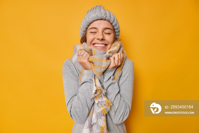 快乐的年轻女人的肖像穿着保暖的衣服，脖子上围着针织帽子围巾，用绸缎闭上眼睛