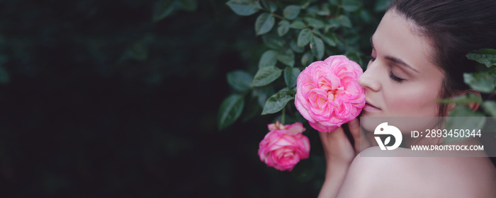 Young beautiful woman portrait close up with perfect skin posing with pink roses flowers in a garden