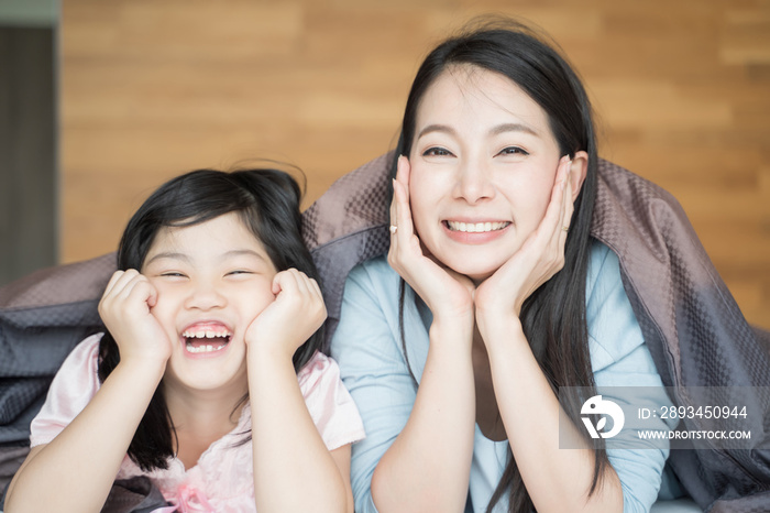 Mother and her daughter child girl playing in the bedroom and putting blanket on . Happy Asian famil