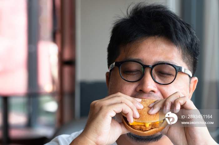 Asia man is eating hamburger in a fast food restaurant and enjoying delicious food. man in a White t