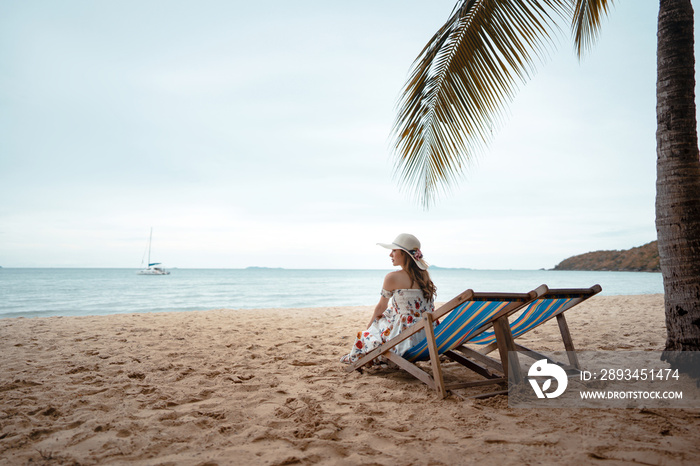 Young asian woman good leisure relax on beach chair with floppy hat under the tree.