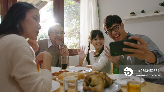 快乐的亚洲家庭的糖果，在家里的餐桌上玩得很开心，在网上进行手机视频通话