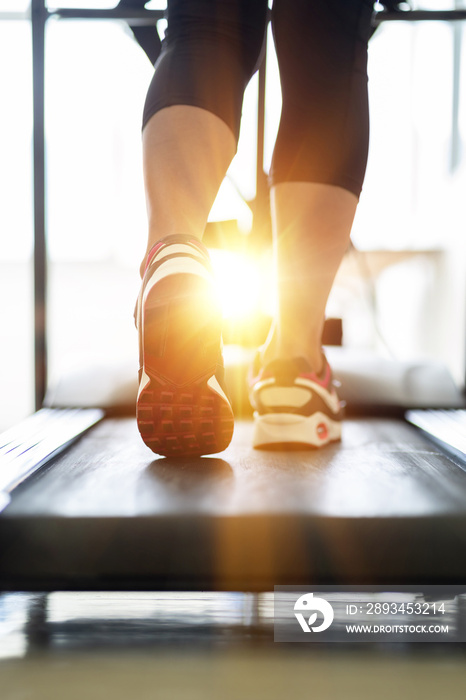 日落时，阳光照射下，健身女性在跑步机上跑步的腿部特写。