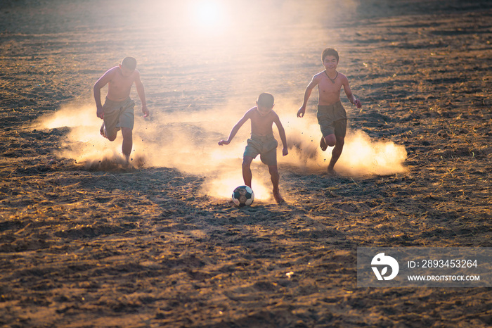 Asian boys friends playing football on the clay ground on summer sunny day. Concept friendship and r