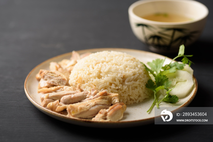 Hainanese chicken rice with coriander, cucumber and chicken soup on black background. Local food in 