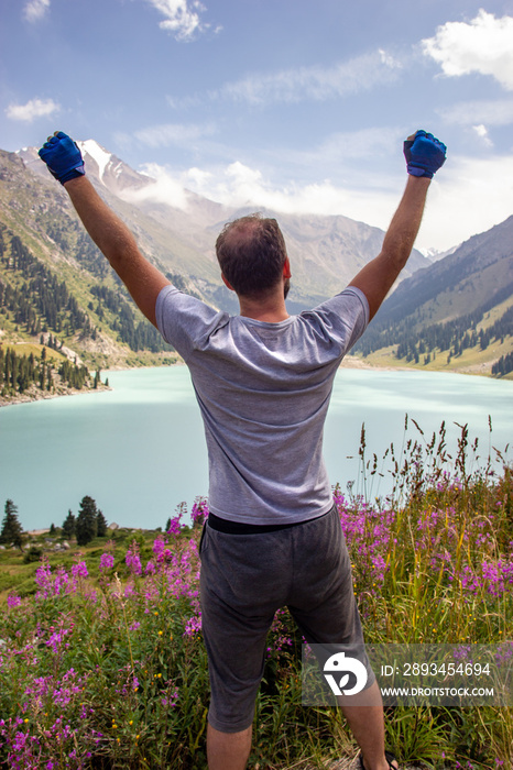 一名男子在山湖旁向天空举起双手。Ti大阿拉木图湖上的壮观景色