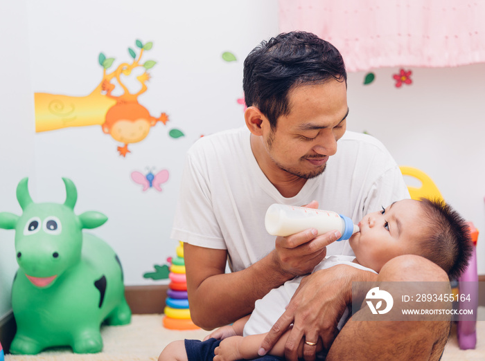 Father acting Mom feeding milk his son baby 1 year old on chair