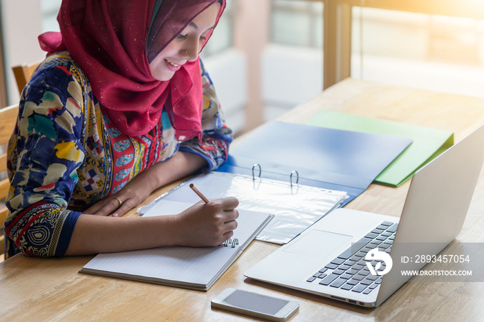 Muslim woman working with computer and writing notebook.