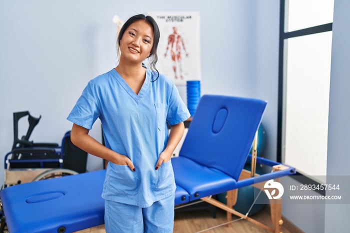 Young chinese woman wearing physiotherapist uniform standing at rehab clinic